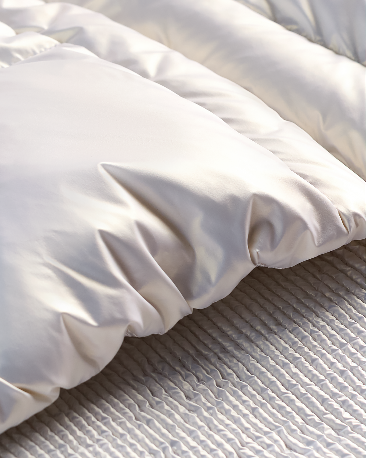 A close-up of a white quilted duvet or comforter with soft folds, resting on a textured light gray or off-white bedspread.