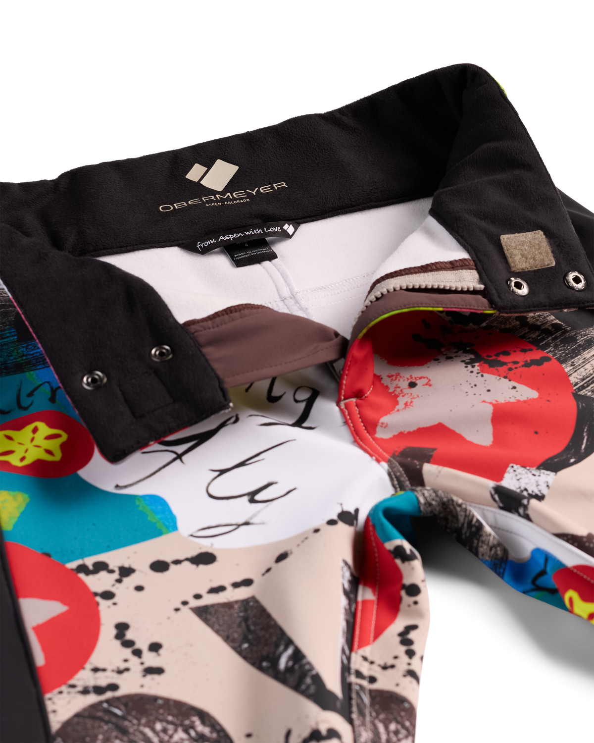 Close-up of a folded collared shirt by Obermeyer, showing a black collar, white inner neck lining, and a colorful abstract print with red, blue, beige, black, and yellow on a white background.