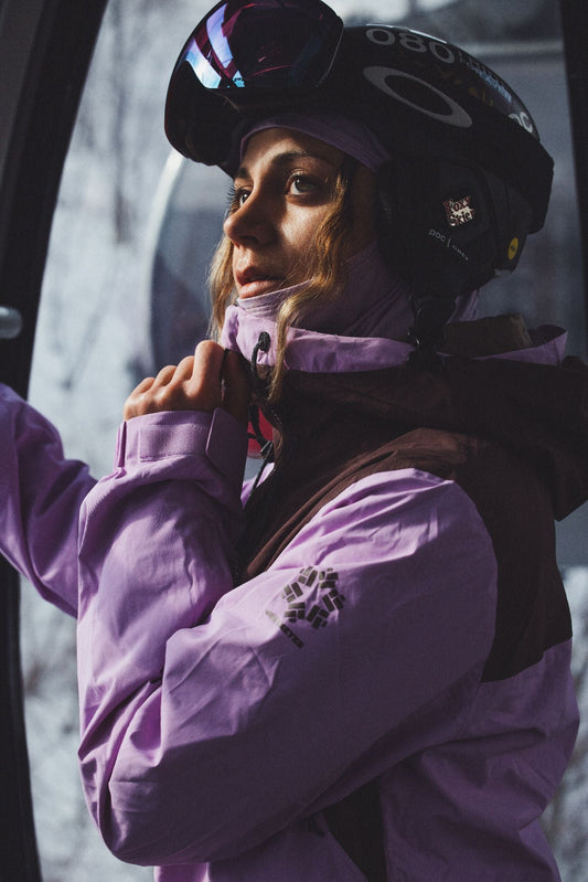 Woman wearing a purple Obermeyer ski jacket and helmet at a ski resort.