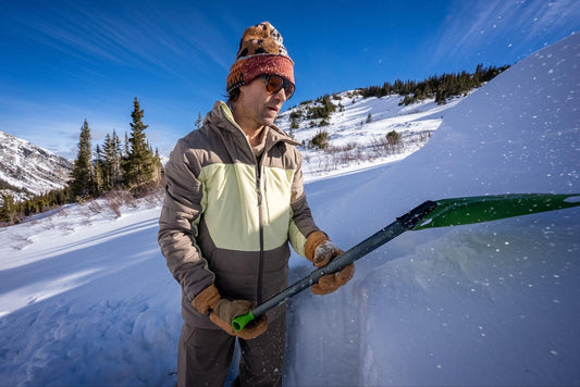 Man wearing a color-block Obermeyer ski jacket while shoveling snow in the mountains.