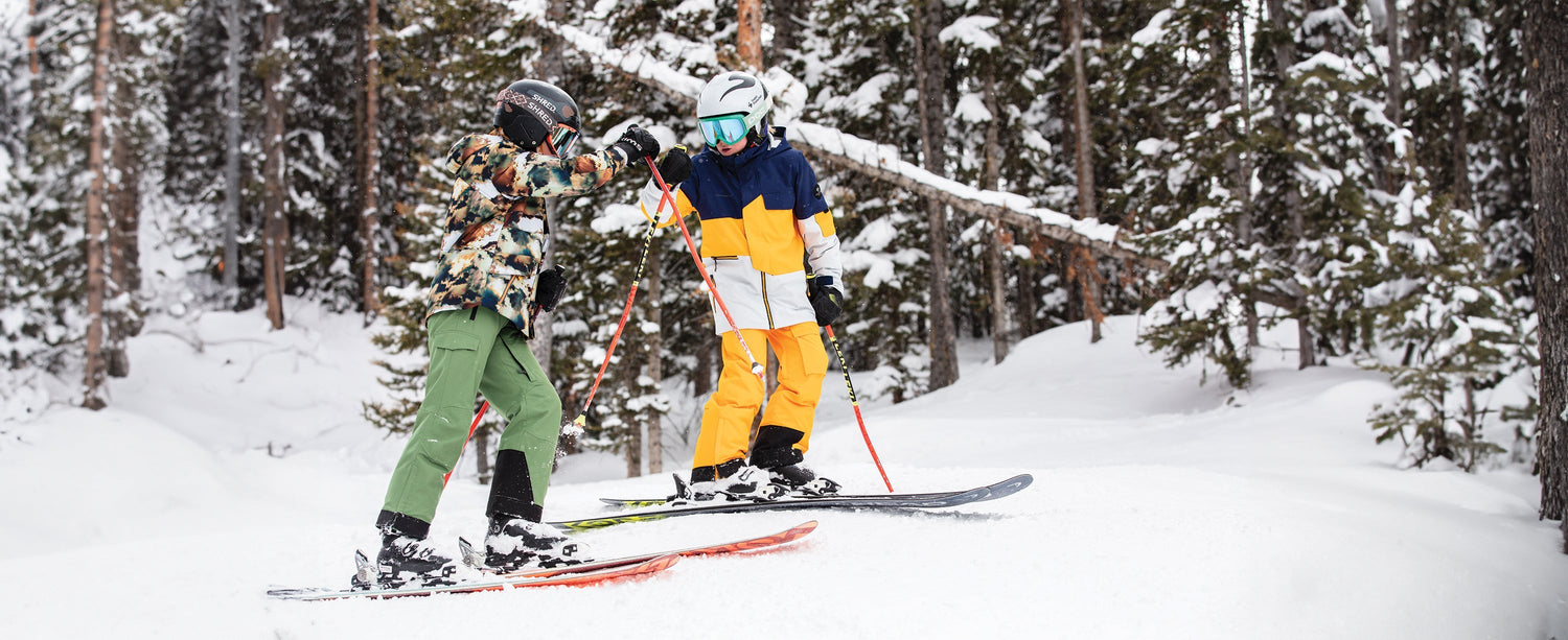 Two teen boy skiers fist bumping while wearing Obermeyer.