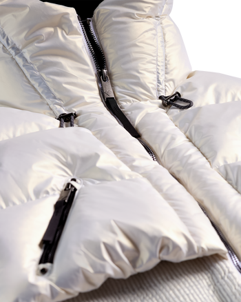 
Close-up of a white puffer jacket with black zippers and silver zipper pulls, showing the padded fabric texture and collar detail.