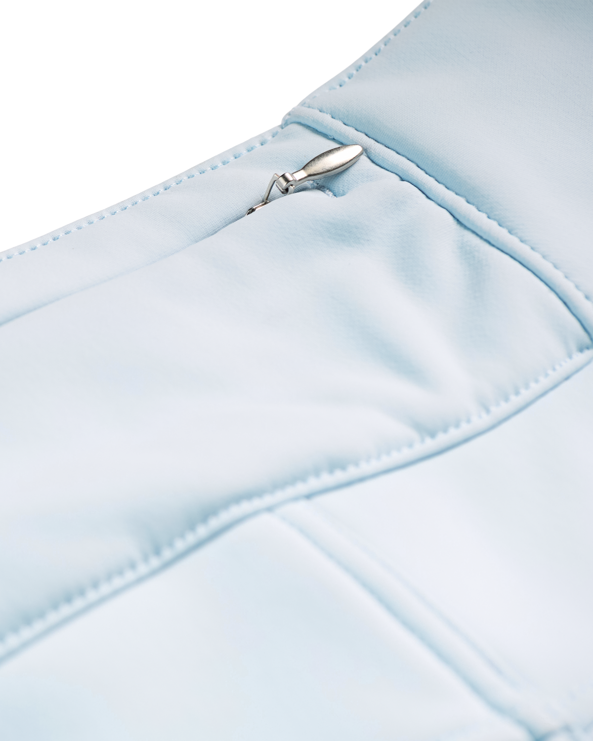 
Close-up detail of a light blue padded garment, showing stitched paneling and a small silver metal zipper pull.