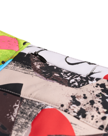 
A close-up of a quilted fabric item, likely a clutch or small bag, featuring a multicolor abstract art print with black, red, pink, green, and beige brushstrokes.
