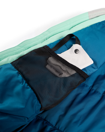 
Close-up of a sleeping bag showing a black mesh pocket holding a white stuff sack, with teal and blue fabric visible.