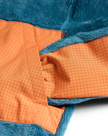 
Close-up of a plush fleece jacket showing a blue teal sherpa exterior and an orange grid-patterned lining.