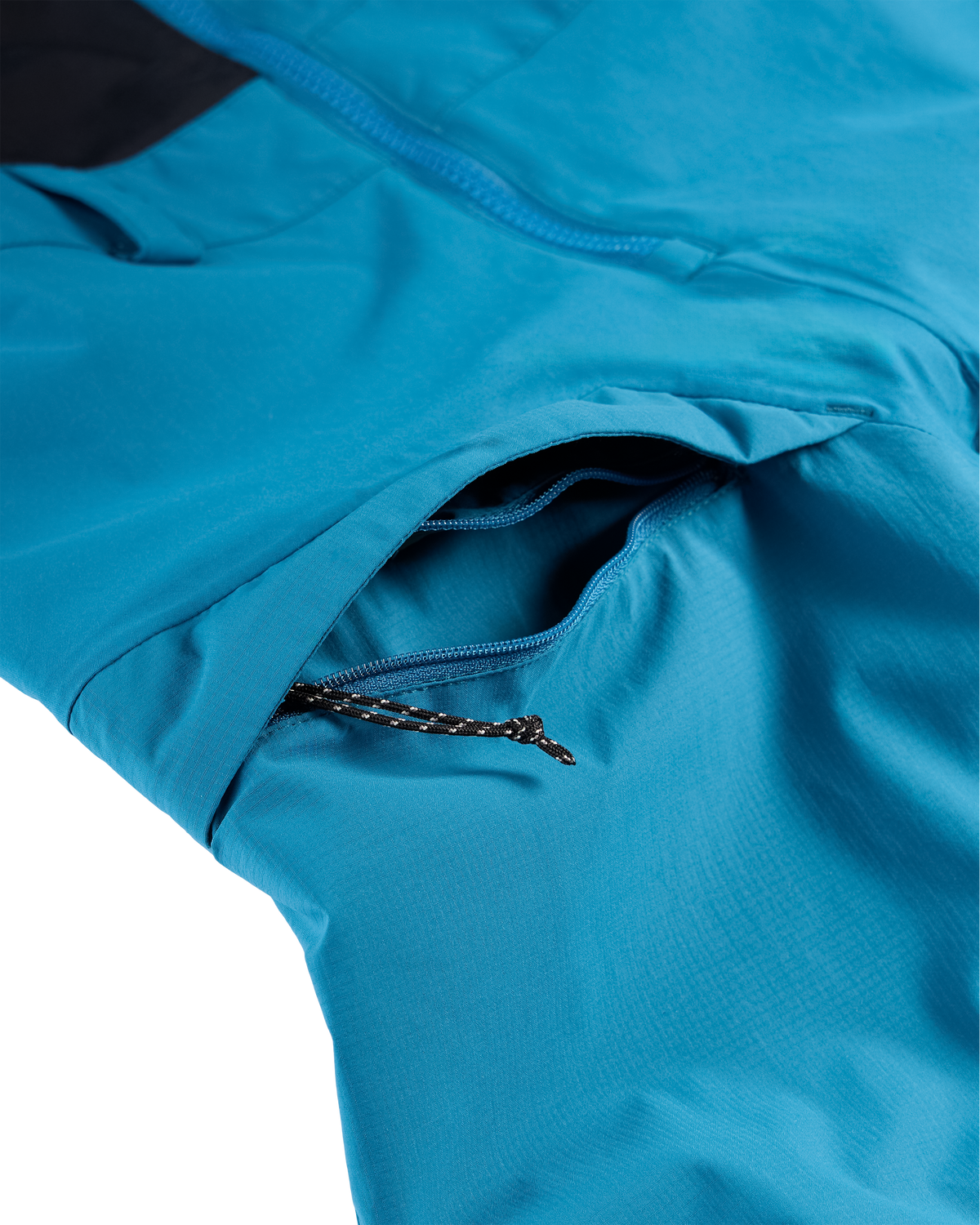 
Close-up of a bright blue technical jacket showing a zippered pocket with a black-and-white braided zipper pull.