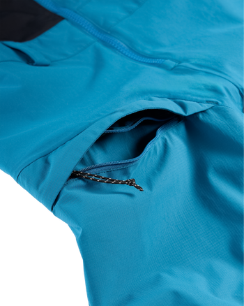 
Close-up of a bright blue technical jacket showing a zippered pocket with a black-and-white braided zipper pull.