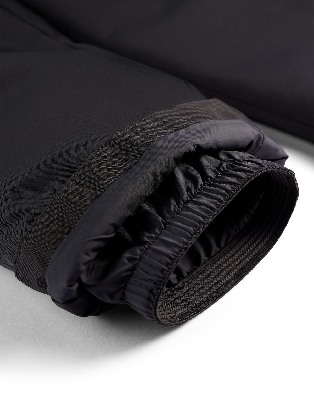 
Close-up of a black insulated jacket cuff with a gathered elastic opening, showing the inner lining and zipper detail on a white background.