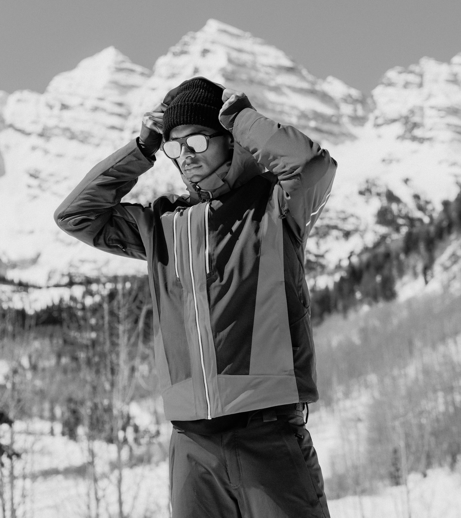 Person wearing a winter jacket and sunglasses with a snowy mountain background