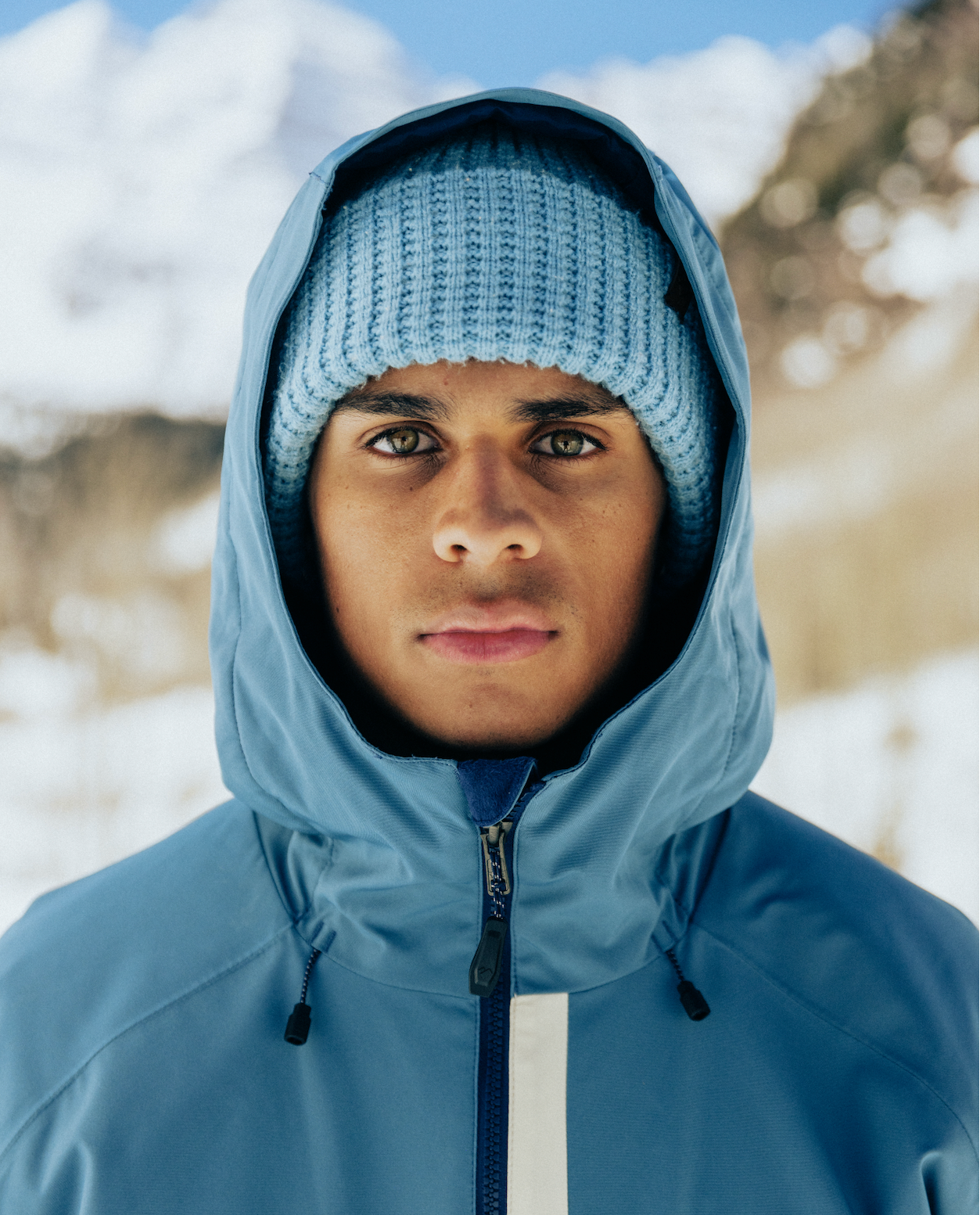 Person wearing a blue Obermeyer jacket and beanie in a snowy mountain setting